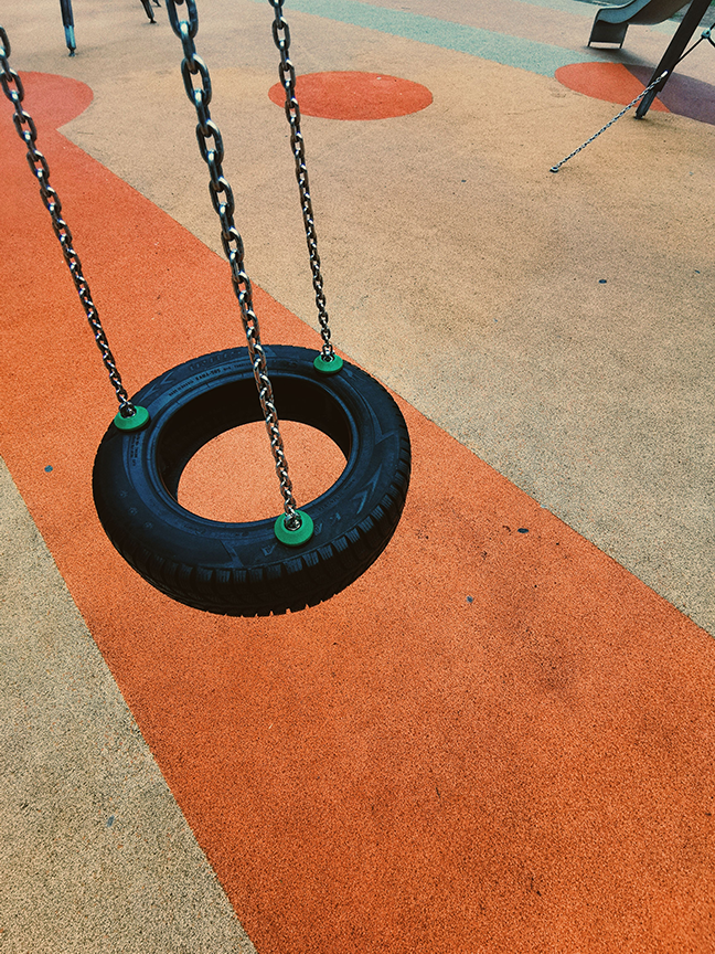 Commercial tire swing mounted on a playground swing frame providing spinning, swinging, and cooperative play opportunities.